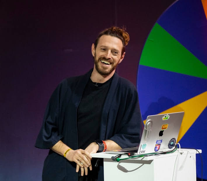 Benji smiling on stage beside a laptop